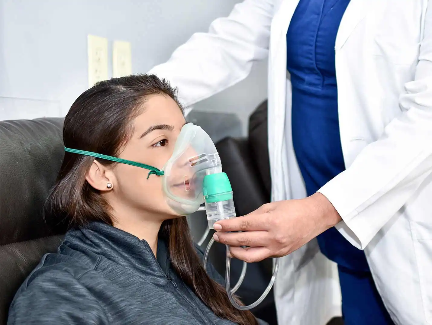 Paciente sentado sobre un sillón y puesta sobre su cara una mascarilla para realizar terapia respiratoria. 